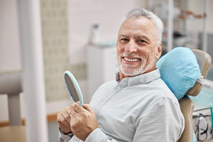 Smiling senior man in dental chair holding mirror