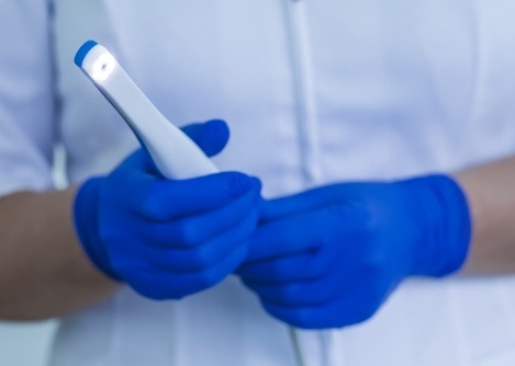 Two gloved hands holding a thin white intraoral camera