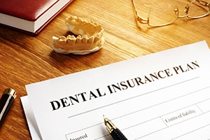 Dental insurance form on desk next to tooth mold and glasses