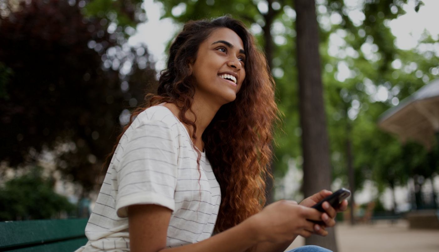 Young woman holding cell phone outdoors with trees in background