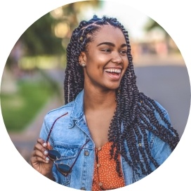 Young woman in denim jacket holding sunglasses and smiling outdoors