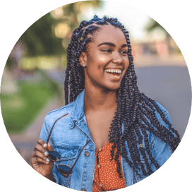 Young woman in denim jacket laughing and holding sunglasses outdoors